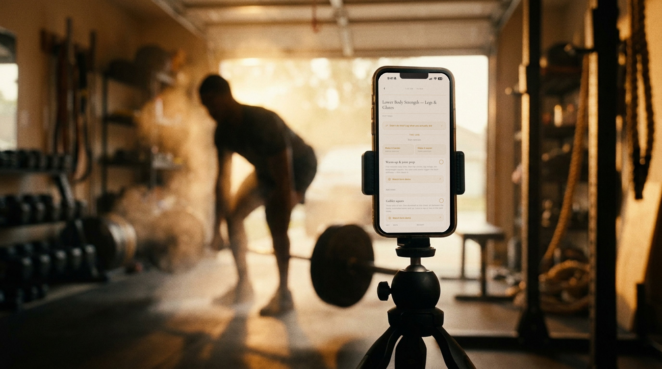 A tripod-mounted phone showing a Resurgo workout block while a man deadlifts in his garage gym